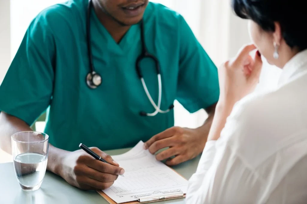 Healthcare professional in scrubs writing on a clipboard during a patient consultation.