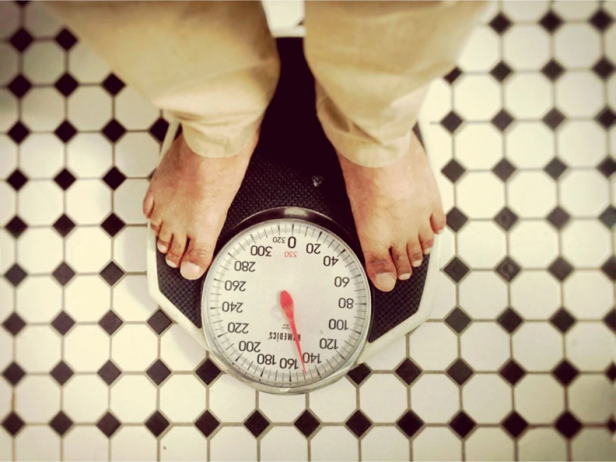 A person standing on a weight scale with a view of the dial, showing weight in pounds.