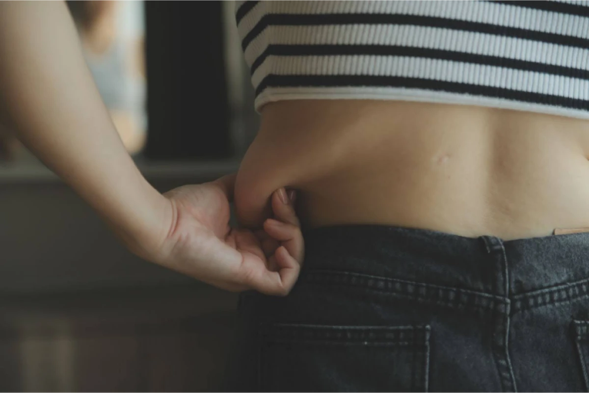 A person pinching their waist to check body fat, wearing a striped crop top and jeans.
