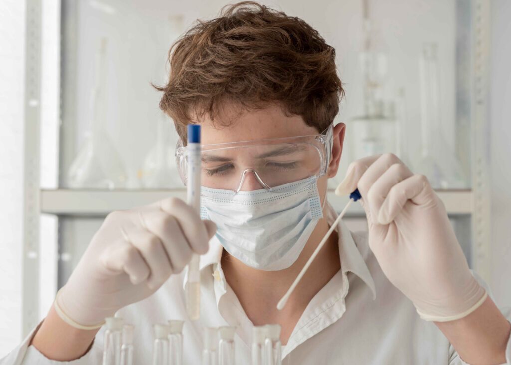 Scientist in mask and goggles working with test tubes.