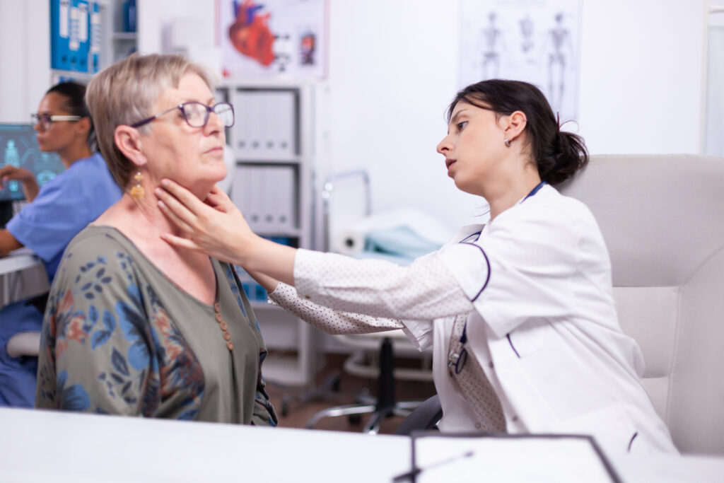 Doctor examining senior woman's neck in clinic.